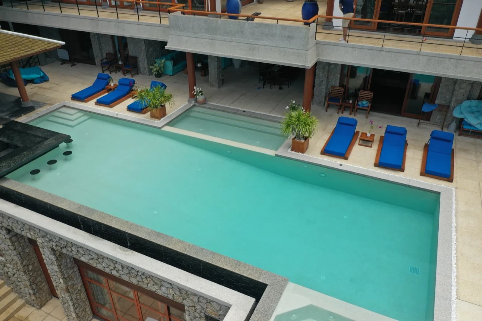 Low oblique aerial along a long aqua pool with sunken bar seating and blue loungers