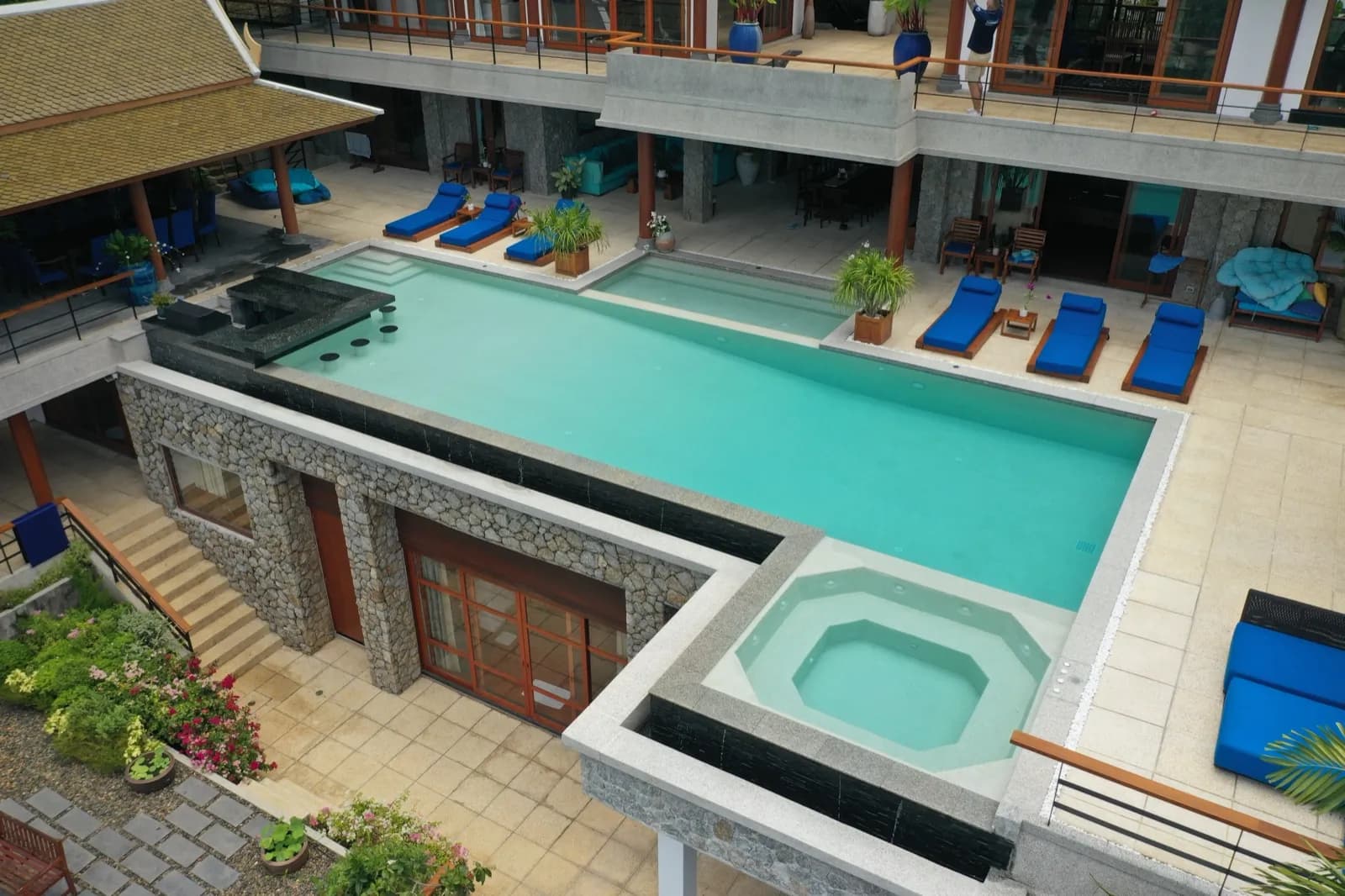 Stone-walled terrace pool and spa beneath a two-storey Thai villa