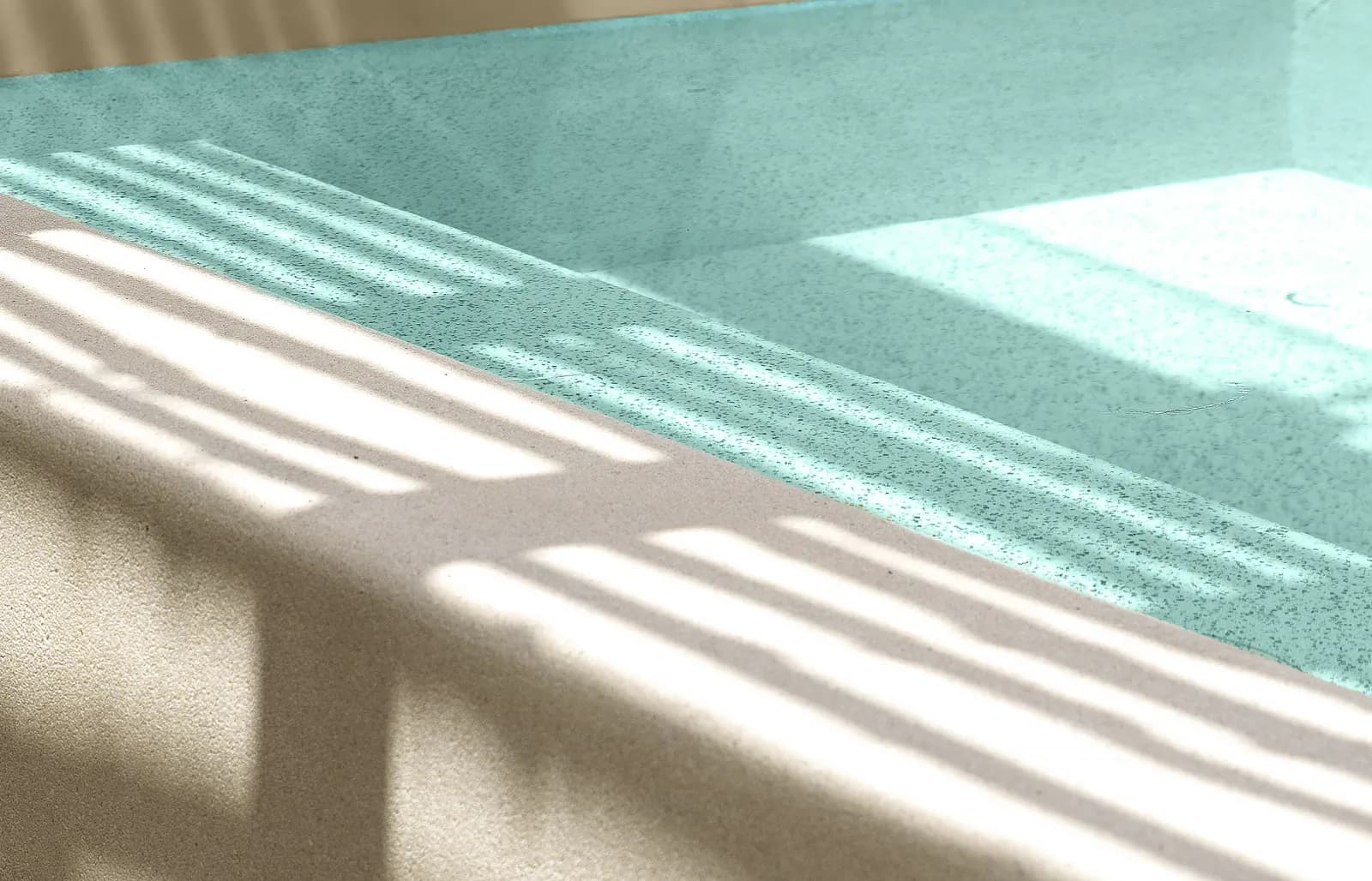 Close-up of a speckled pebble pool finish under clear water with stripes of sunlight