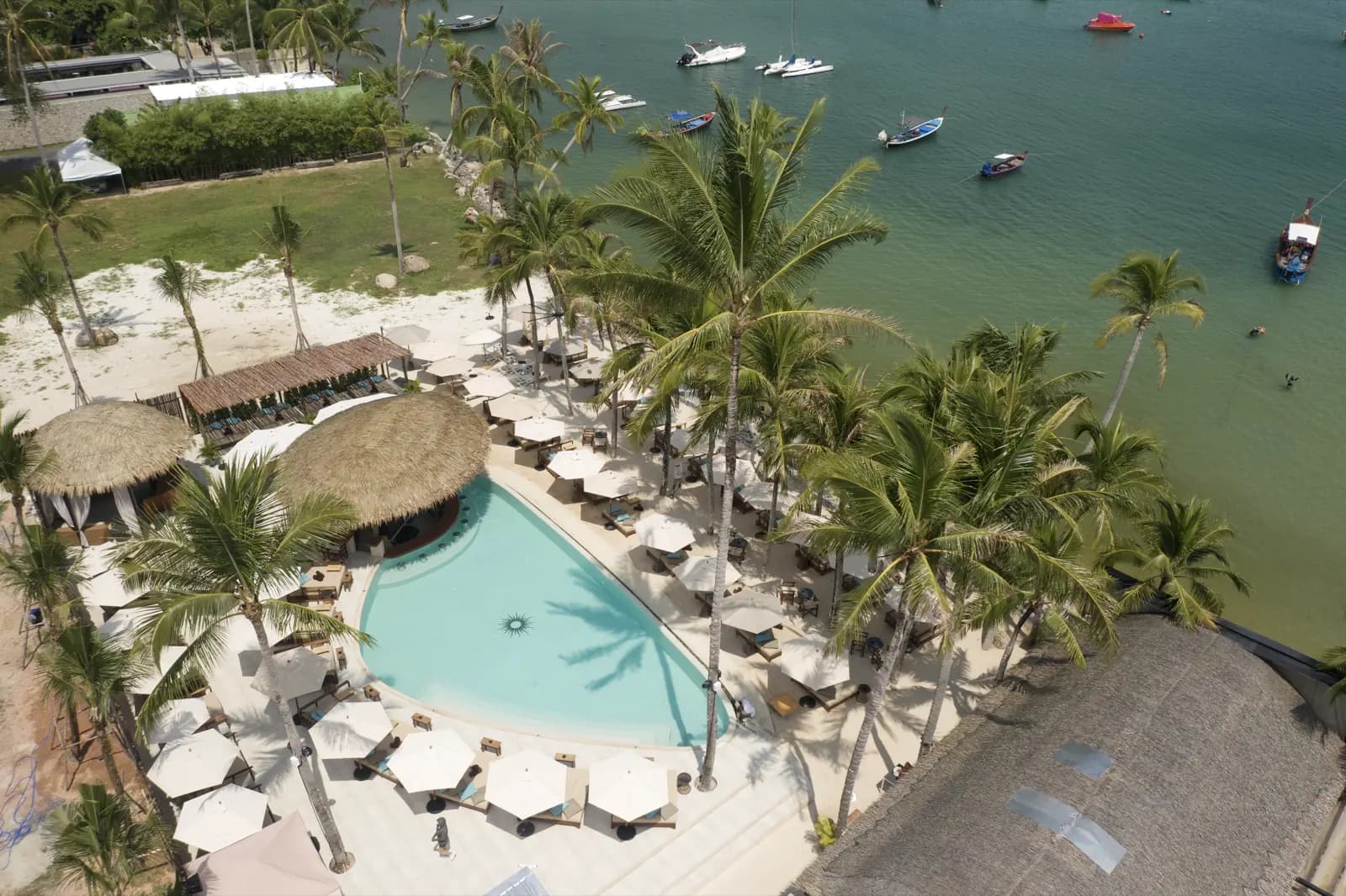Finished beach club pool on the shoreline with boats moored in the bay