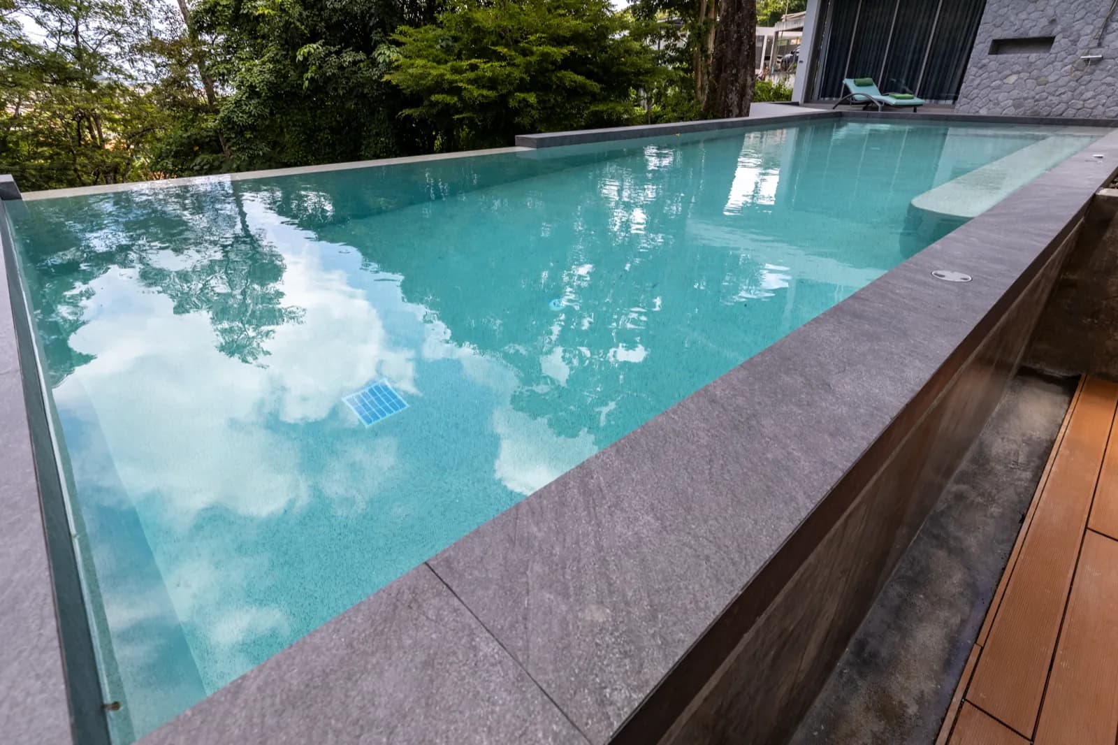 Overflow pool edge mirroring clouds and treetops above light aqua water