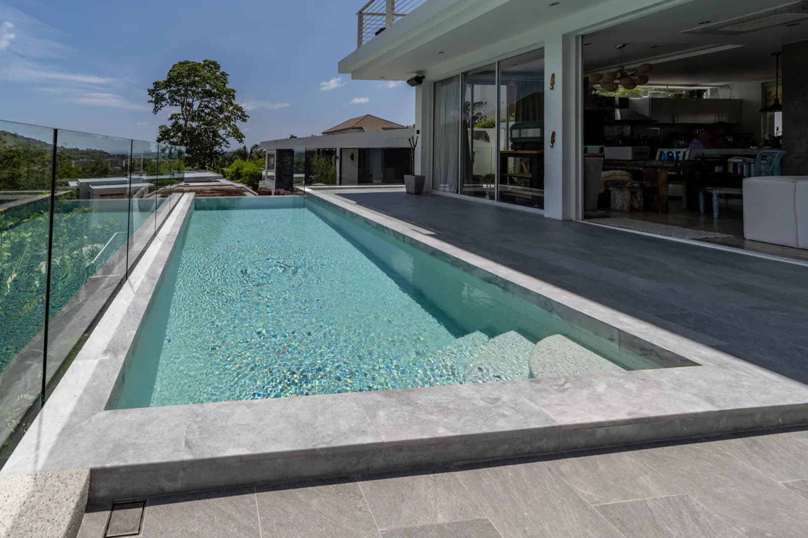 Lap pool running alongside an open-plan living room and grey stone terrace