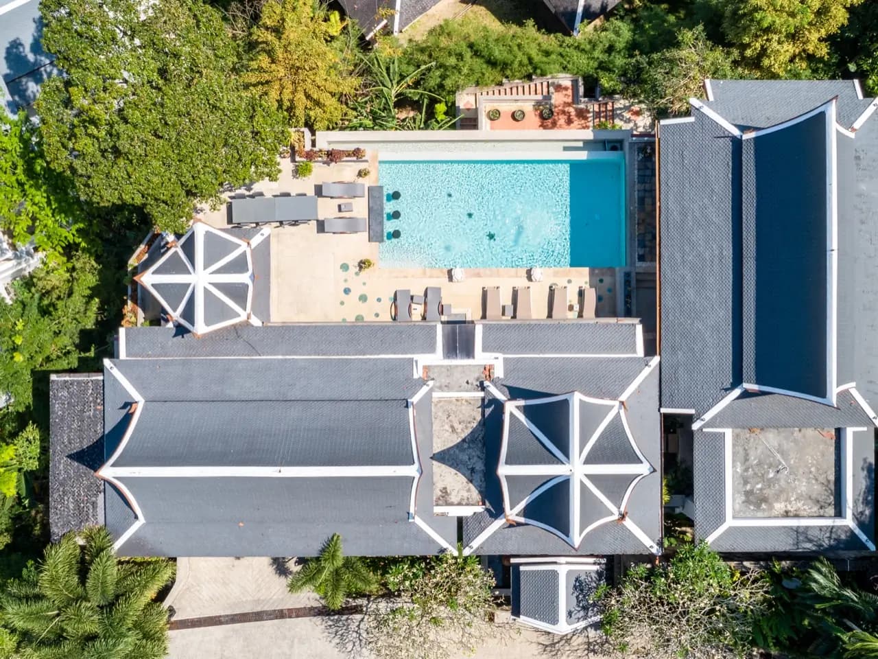 Top-down drone view of a light-aqua pool beside Thai rooftops