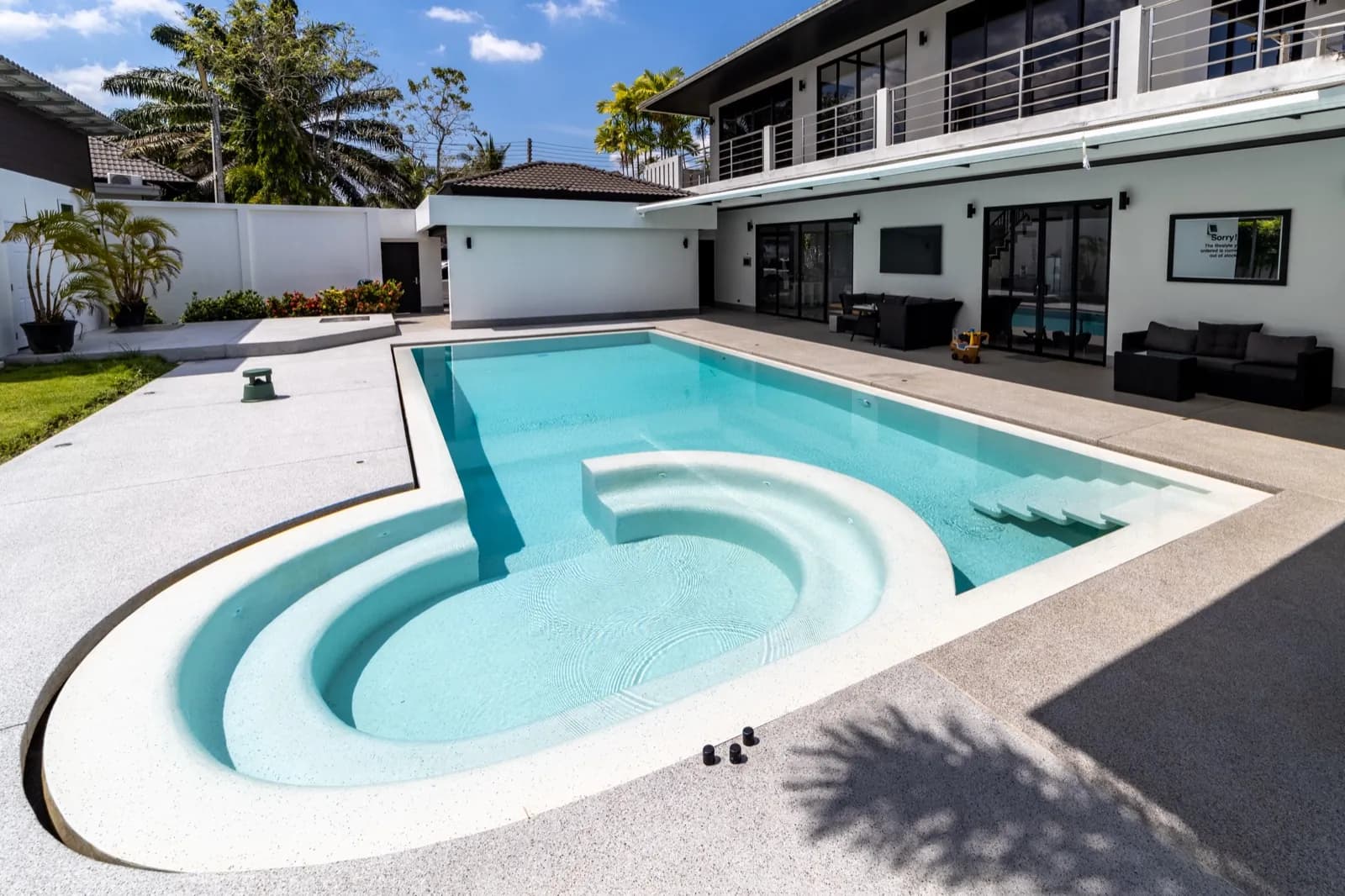 Keyhole pool with curved steps and palm shadows beside a modern villa