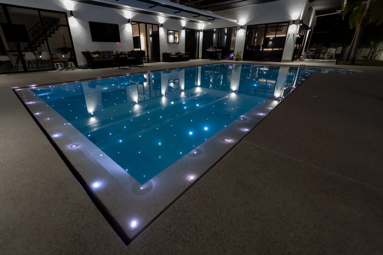 Pool at night reflecting the villa's wall lights, with starlight points in the floor
