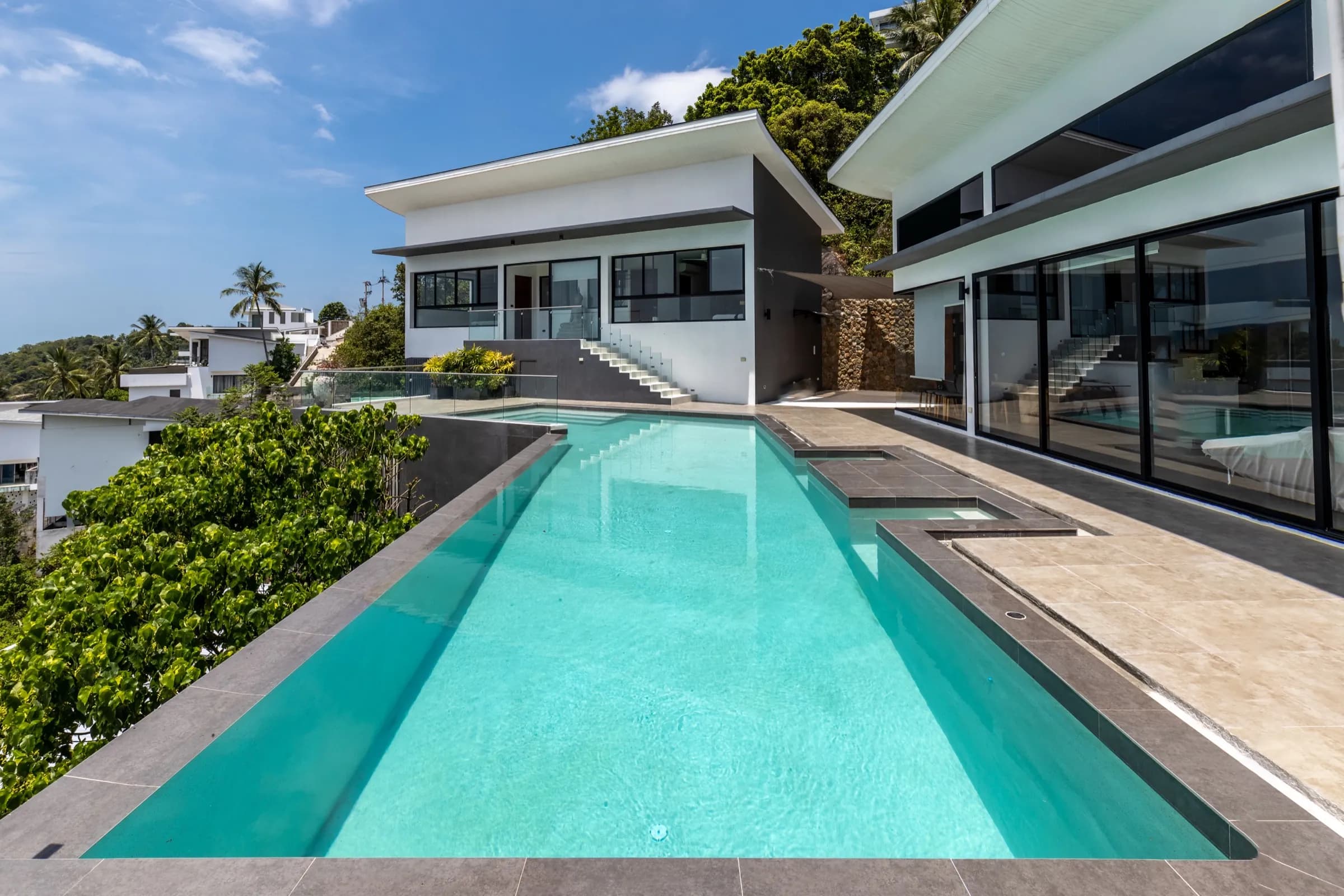 Turquoise lap pool leading to a contemporary white villa with floor-to-ceiling glass