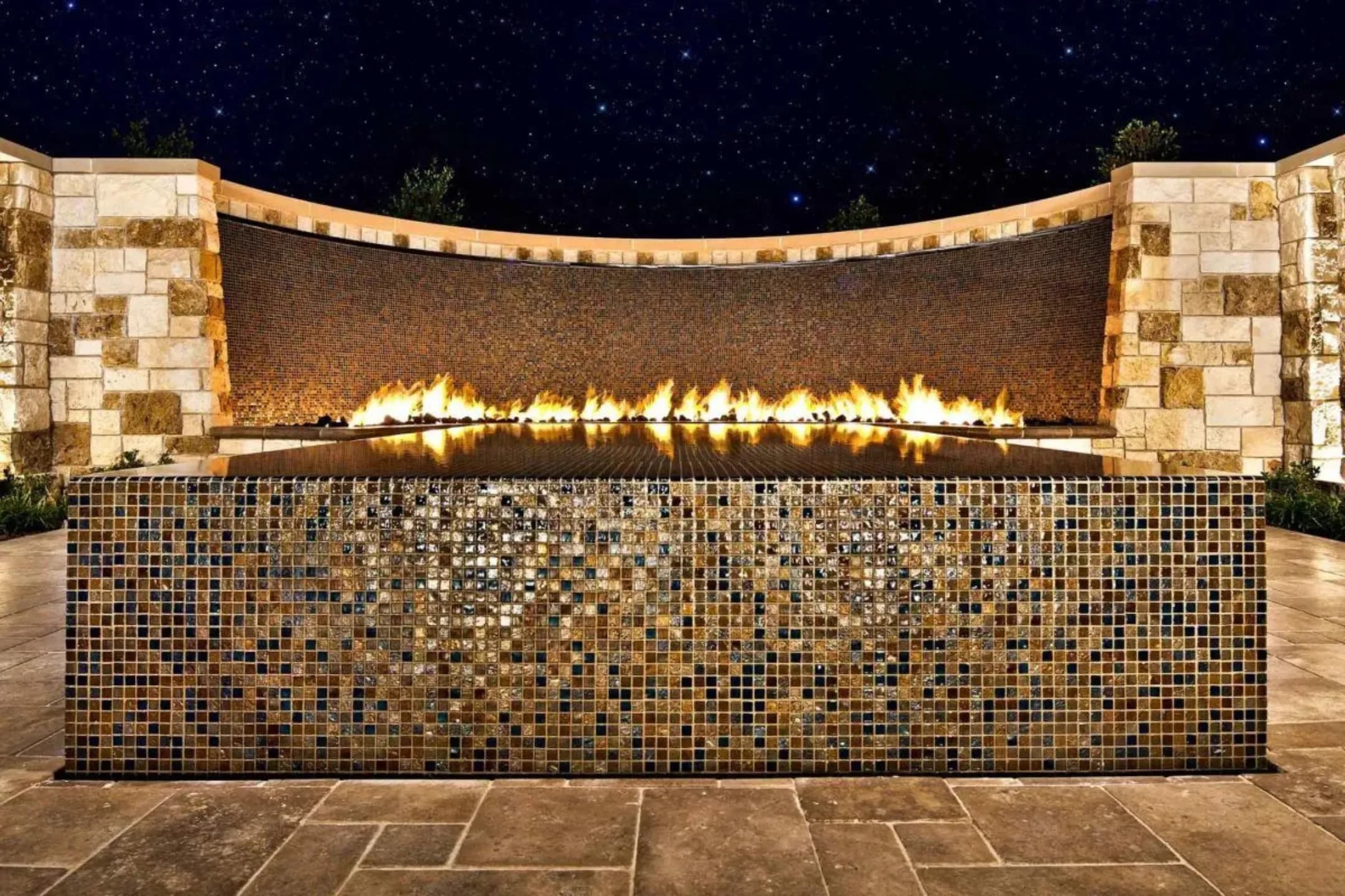 Fire feature wall clad in bronze Lightstreams glass tile at night
