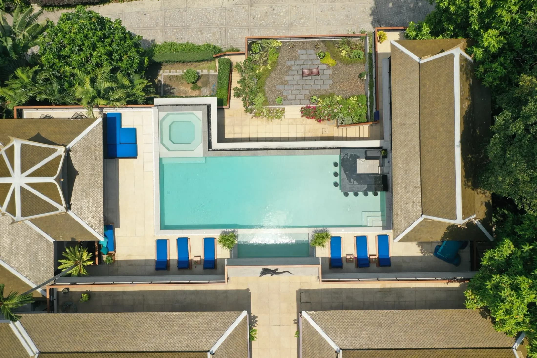 Top-down drone view of a Thai-style villa courtyard with a turquoise pool, spa and flowing cascade