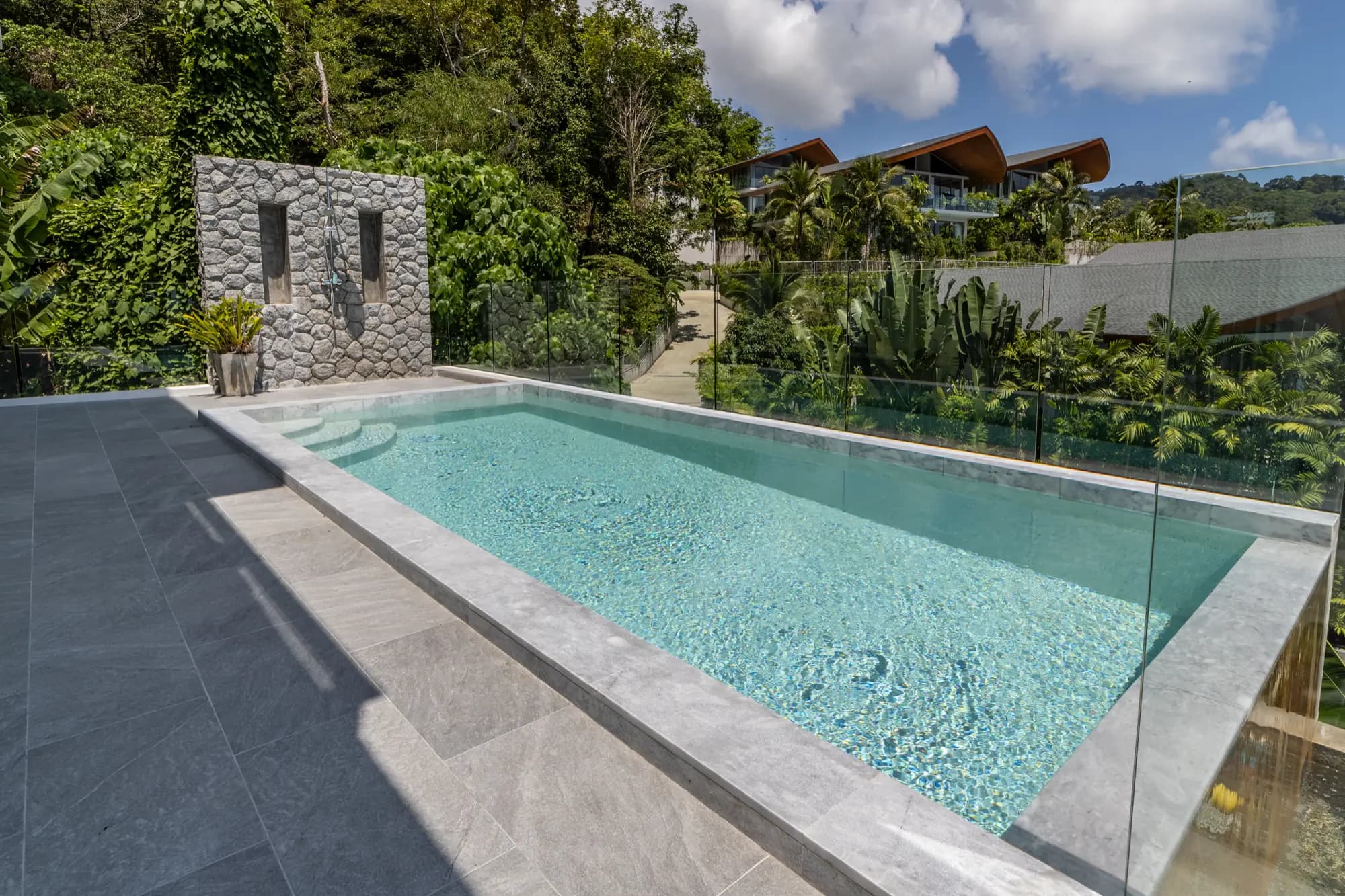 Glass-edged hillside pool with a stacked-stone feature wall and jungle backdrop