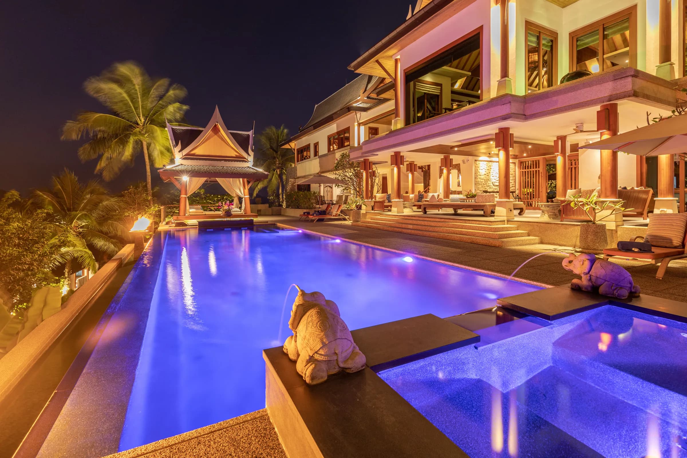 Thai villa pool at night glowing violet-blue, with elephant fountains and a lit sala pavilion