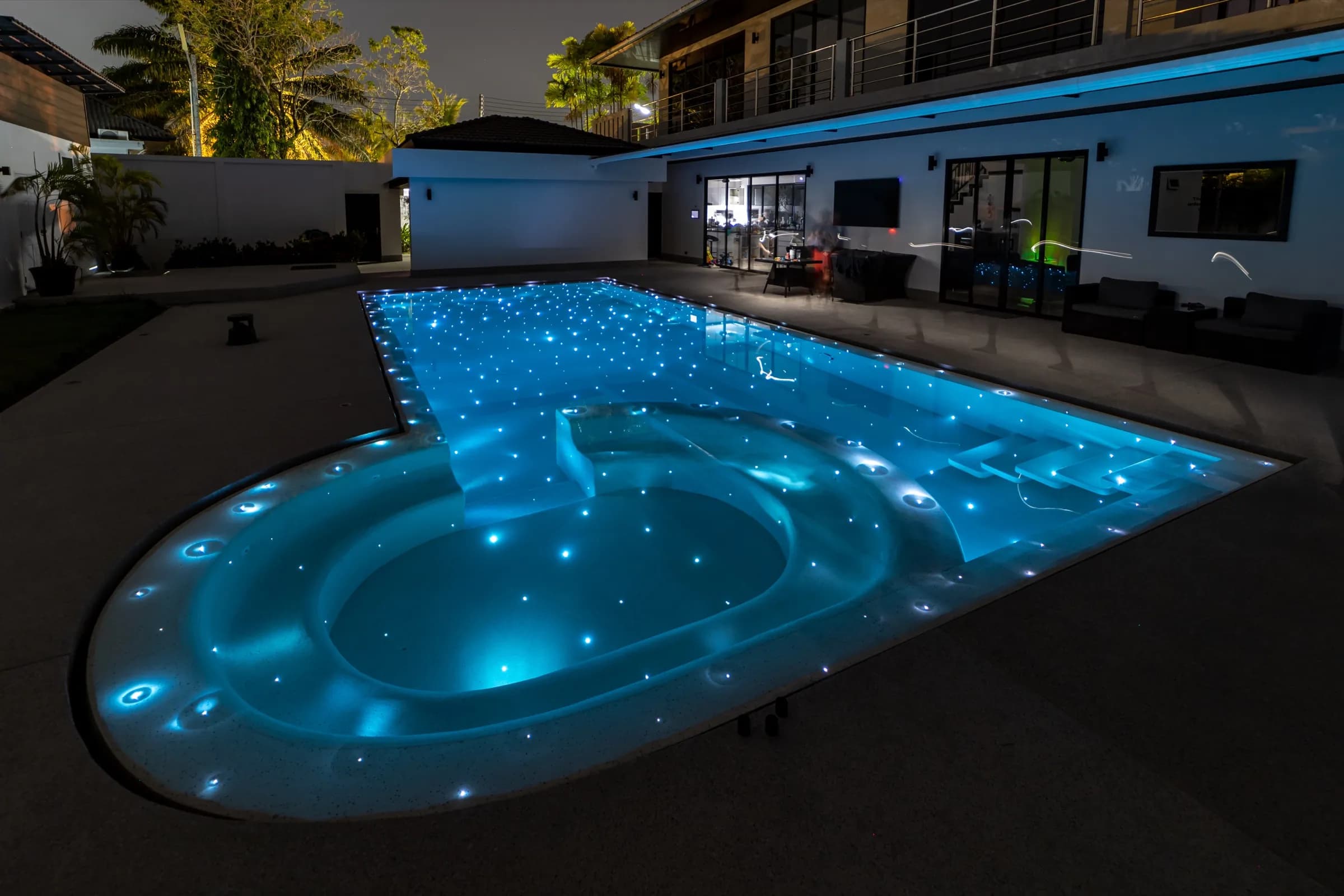 Keyhole-shaped pool glowing cyan at night with fibre-optic starlight points across the floor