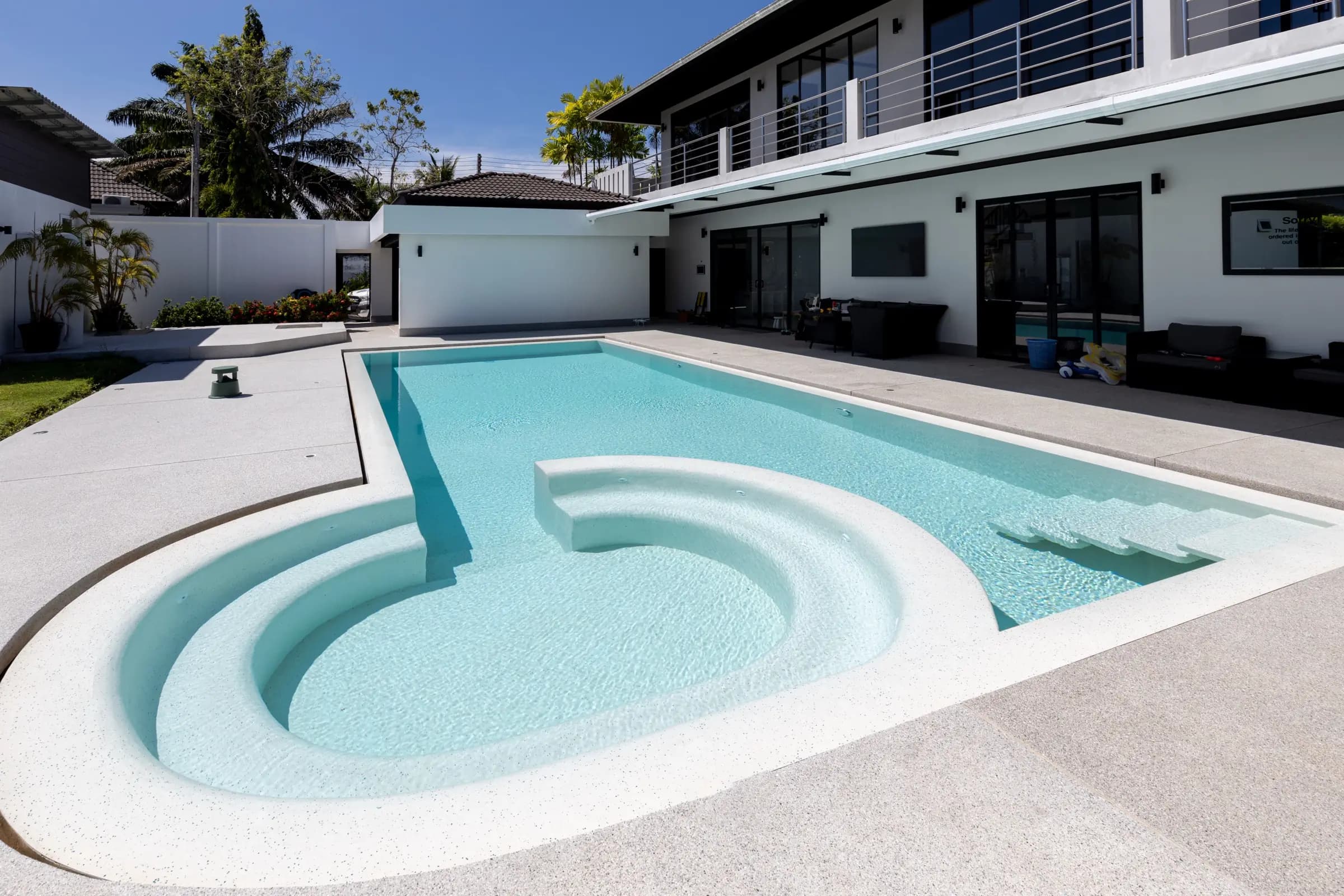 Sculpted curved lounge steps of a bright aqua pool in front of a modern white villa