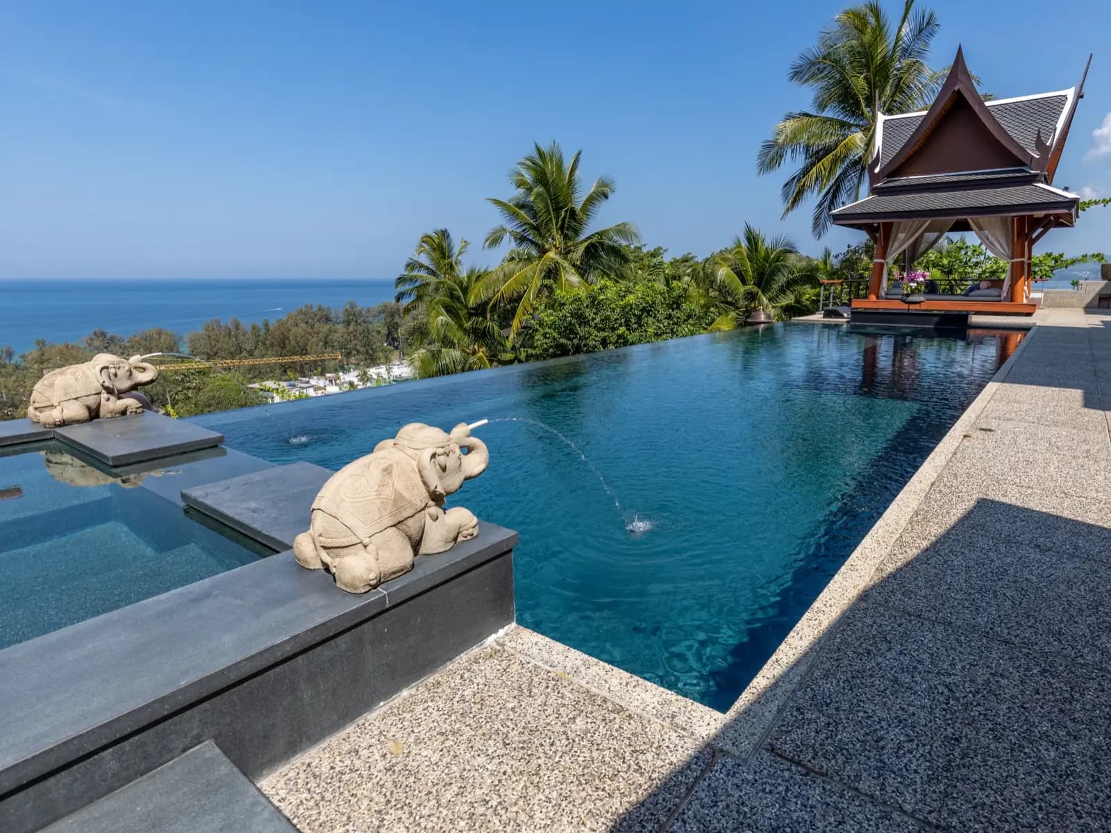 Stone elephant spouting water into a dark infinity pool overlooking the sea