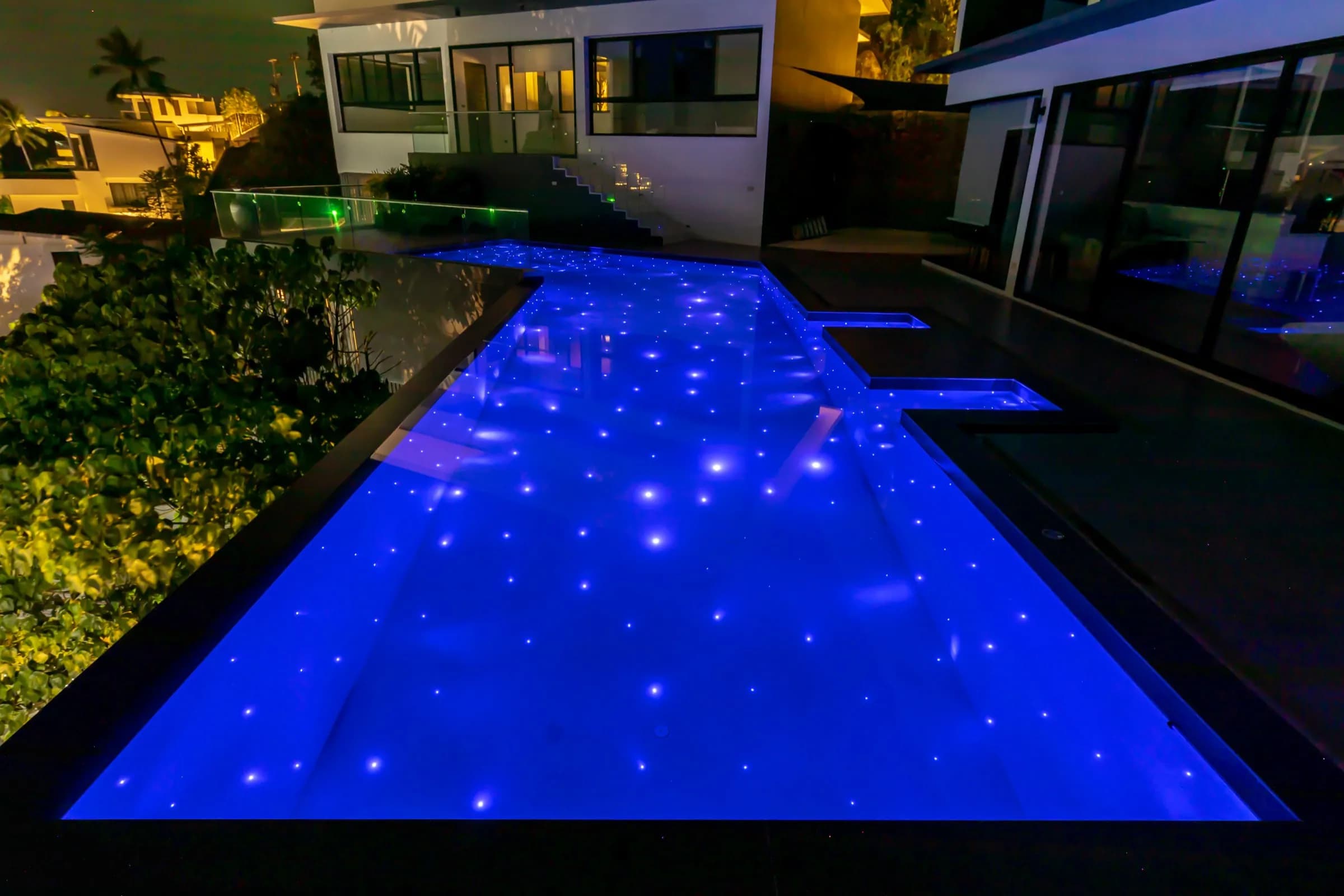 Villa lap pool glowing deep blue with fibre-optic star lights at night
